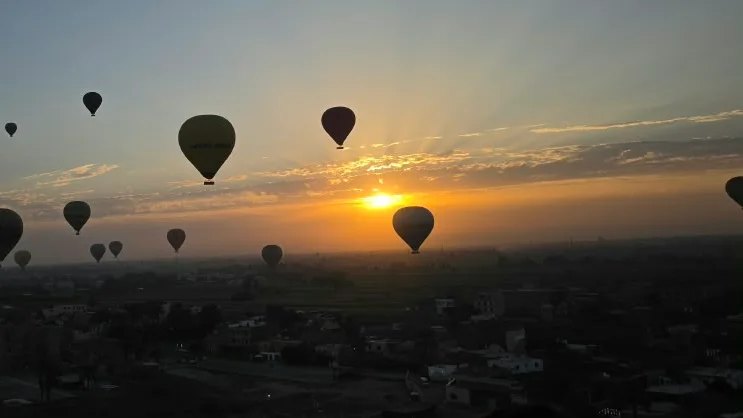 Mongolfiere controluce mentre il sole sale sull'orizzonte di Luxor
