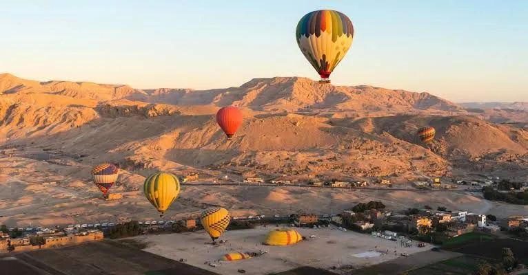 A fleet of hot-air balloons rising over the Nile valley and temples of Luxor at dawn