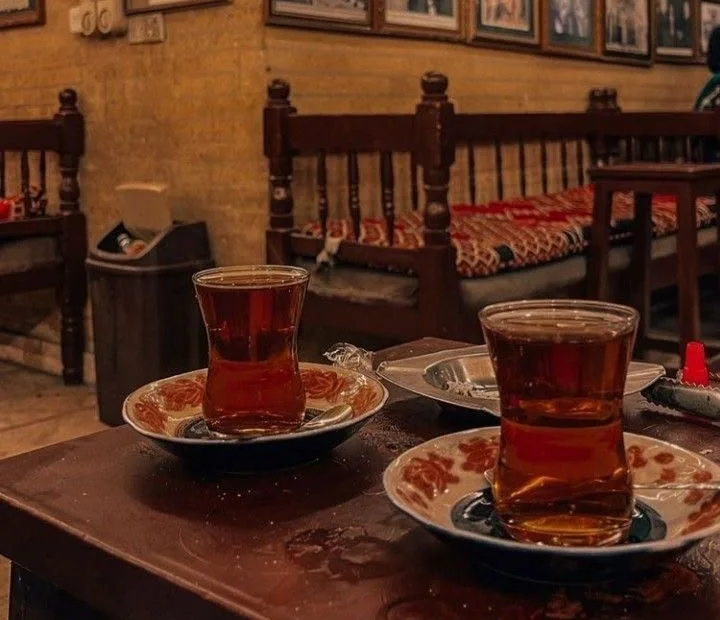 Dua gelas teh di meja sebuah kedai kopi tradisional yang dindingnya penuh foto-foto lama berbingkai