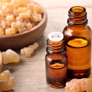 Tears of frankincense in a wooden bowl, beside bottles of frankincense oil